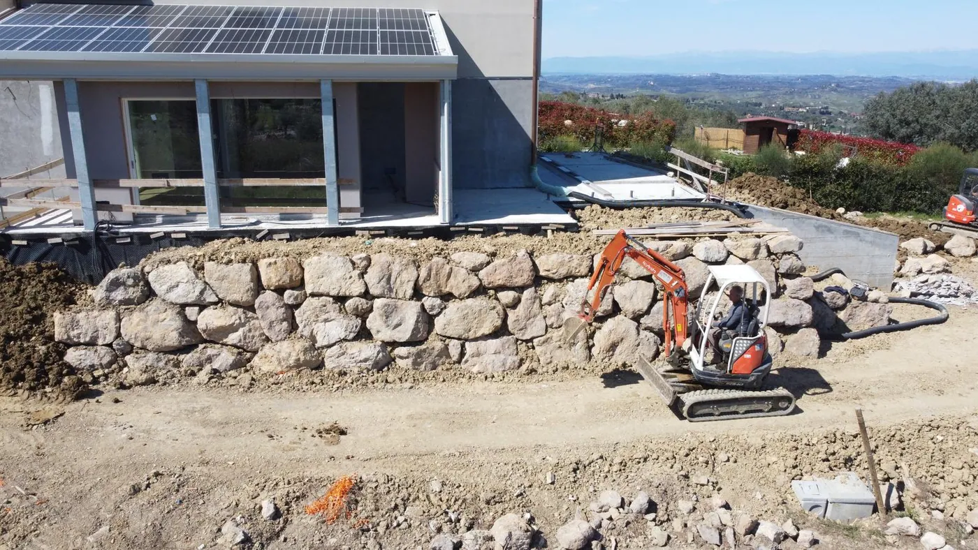 Realizzazione di scogliera a secco con massi naturali per il contenimento e la sistemazione del terreno in pendenza.  L’intervento ha permesso di sostenere il dislivello e regolarizzare la scarpata, creando al tempo stesso una soluzione solida e ben integrata nel contesto esterno dell’abitazione. La posa dei massi è stata eseguita curandone disposizione e incastro, così da ottenere un’opera funzionale e dall’aspetto naturale.  Ideale per: contenimento di scarpate, sistemazioni di terreni in pendenza, giardini, accessi e aree esterne.