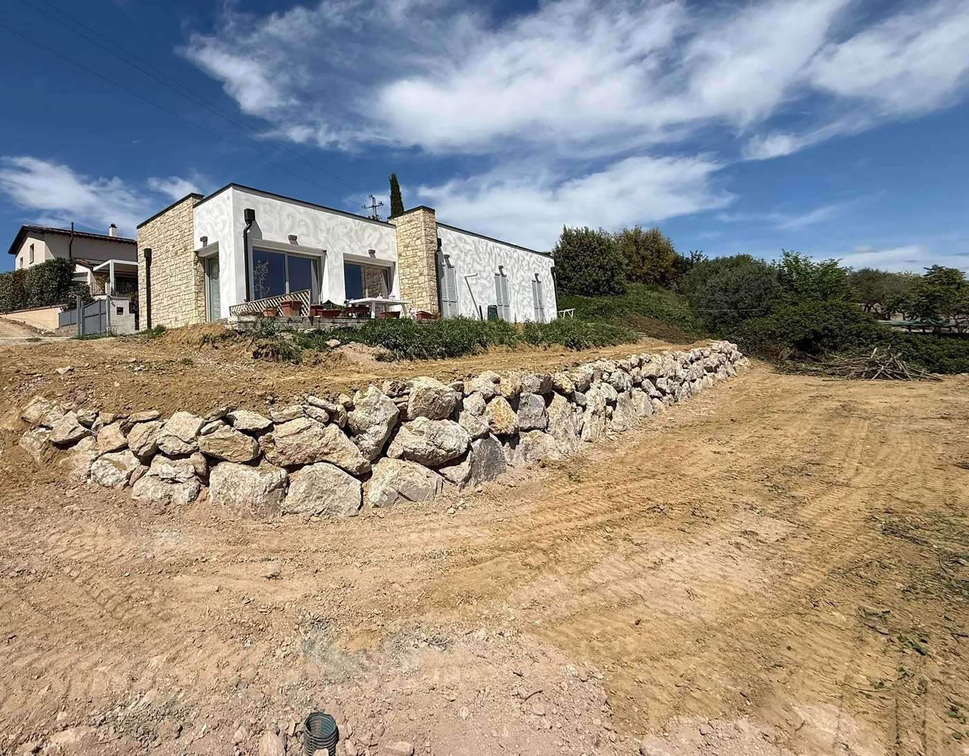 Realizzazione di scogliera a secco con massi naturali per il contenimento e la sistemazione del terreno in pendenza.  L’intervento ha permesso di sostenere il dislivello e regolarizzare la scarpata, creando al tempo stesso una soluzione solida e ben integrata nel contesto esterno dell’abitazione. La posa dei massi è stata eseguita curandone disposizione e incastro, così da ottenere un’opera funzionale e dall’aspetto naturale.  Ideale per: contenimento di scarpate, sistemazioni di terreni in pendenza, giardini, accessi e aree esterne.